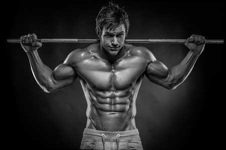 Muscular bodybuilder guy doing exercises with dumbbells over black backgroundの写真素材