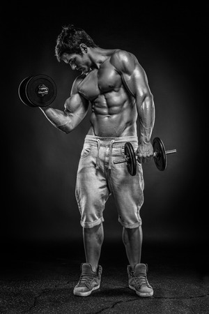 Muscular bodybuilder guy doing exercises with dumbbells over black backgroundの写真素材