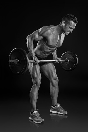 Muscular bodybuilder guy doing exercises with big dumbbell over black backgroundの写真素材