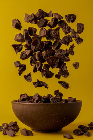 Levitating Chocolate Pieces Above Bowl on Vibrant Yellow Background for Culinary Concepts AI Generativeの素材