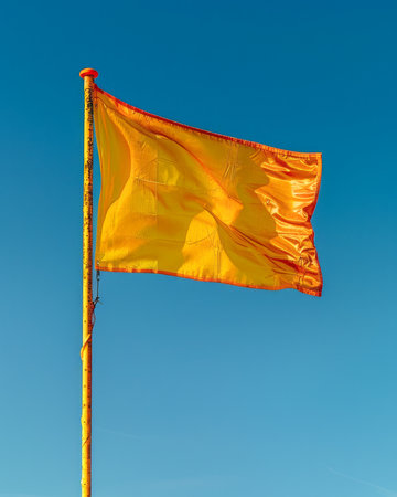 Bright Yellow Flag Fluttering Against Clear Blue Sky, Vibrant Outdoor Symbol, Conceptual Image of Hope and Positivity in Natural Environment, Colorful Banner Waving in the Wind on Sunny Day, Close Up AI Generativeの素材