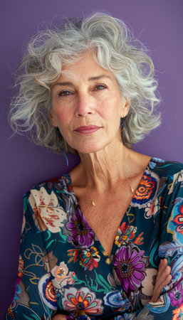 A confident mature woman with silver hair and a floral blouse looks directly at the camera with a serious expression  The background is a vibrant purple  This photo is perfect for projects related to aging, beauty, confidence, or women's empowerment AI Generativeの素材