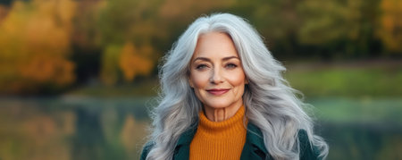 Bathed in dawn's golden light, a poised elderly woman with flowing silver hair exudes timeless beauty and inner strength Her serene expression, gentle smile, and expressive eyes are highlighted against a tranquil autumnal backdrop The portrait captures the grace and elegance of aging, celebrating natural beauty and peaceful reflection AI Generativeの素材