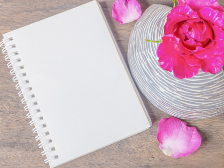 Notepad and pink rose in vase on wooden tableの写真素材