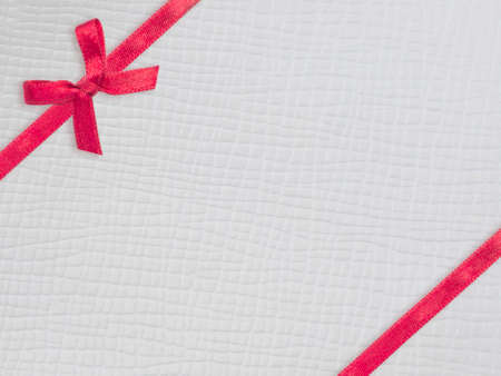 Red ribbon and bow on white leather texture backgroundの写真素材