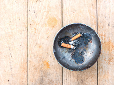cigarette and metal ashtray on dirty wooden tableの写真素材