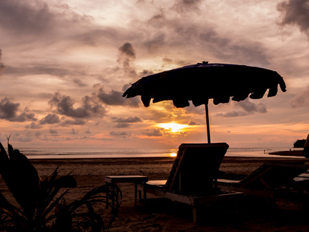 Silhouette beach chairs with umbrella at sunsetの写真素材