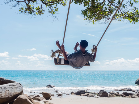 Young man swinging in a swing on tropical summer beachの写真素材