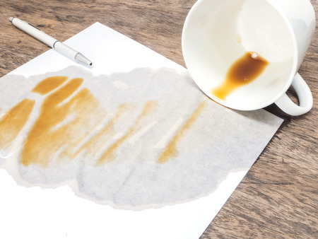 coffee spilled out from white cup on white paper and wooden backgroundの写真素材