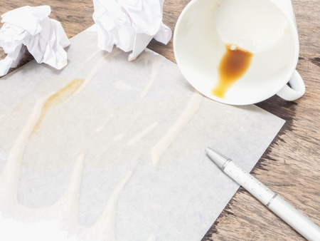 coffee spilled out from white cup on white paper and wooden backgroundの写真素材