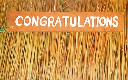 Congratulations letters on wooden board over  straw background