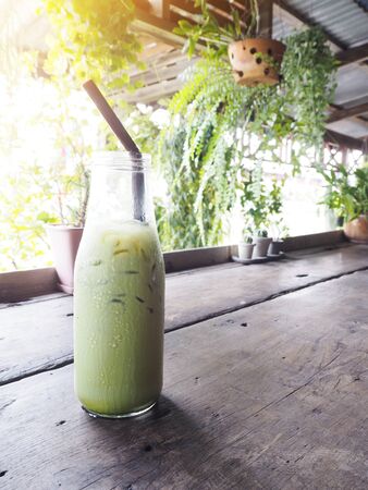 Bottle of ice green tea with straw on wooden table at sunrise.の写真素材