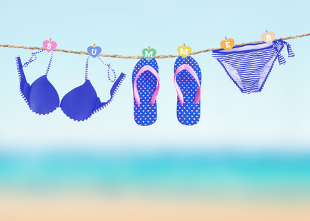 Fashionable woman swimming suit and flip flop hanging on clothesline over blury summer beach backgroundの写真素材