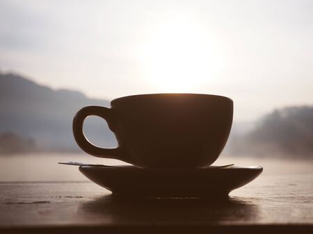 Silhouette cup of coffee at sunrise in the morning over mountain and lake background.の写真素材