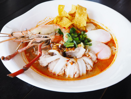 white bowl of Tom Yum Kung with noodles and seafood isolated on wood background, popular Thai food.の写真素材