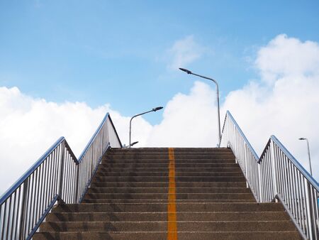 Concrete stair of footbridge with yellow line over blue sky and white clouds background