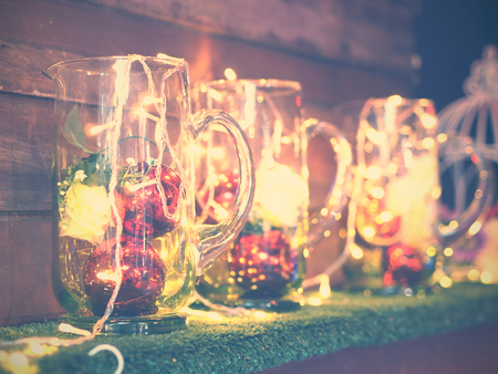 Ornament for christmas party decoration. Glitter balls and rose flower in vases with small light bulbs on grass shelf. Vintage filter effect.の写真素材