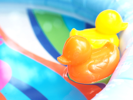 Small orange and yellow plastic duck toys floating on water in children's swimming pool.の写真素材