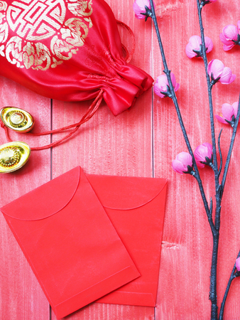 Ornament of Chinese New Year card. China good luck symbol and small pink blossom flower on red wooden background. Envelope and silky money bag on pine wood.の写真素材