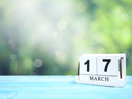 Happy St Patricks Day save the date concepts. White vintage wood calendar on blue wooden table over abstract green bokeh background.の写真素材