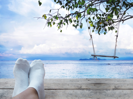 Selfie feet on wooden vintage floor over wood swing hanging under big tree at summer beach and blue sky background. Relaxtion on vacation concept. の写真素材
