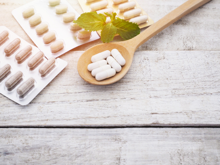 Close up white herbal pills in wooden spoon with blister package and mint leaf on vintage wood grunge background with copy space.の写真素材