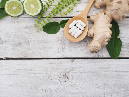 herbal pills in wooden spoon with ginger root, Kaffir lime fruit and basil flower on wood background with copy space. Above view.の写真素材