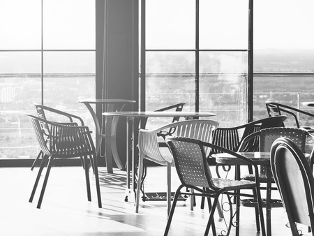 Metal chairs and table at coffeeshop near glass window with cityscape aerial view background, black and white color.の写真素材