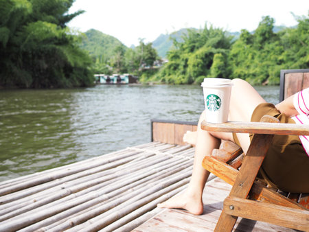 KANCHANABURI, THAILAND - JUN 24, 2018 : Starbucks take away coffee cup on the chair at the resort nearby the river in the morning.のeditorial素材