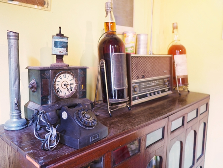 Vintage things for room decoration. Close up antique clock, old whisky, radio, lamp and telephone on wooden cabinet.の写真素材