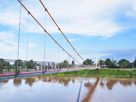 Suspension sling bridge named Sawanvoranayokramluk across Yom river against blue sky at Sukhothai province, Thailand.の写真素材