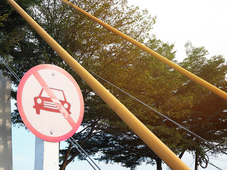 Close up white and red no car allowed sign in front of narrow sling bridge.