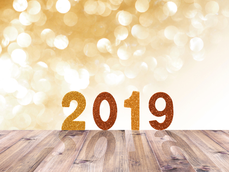 Wooden table top and 2019 New year glitter number over gold abstract blured background and white...
