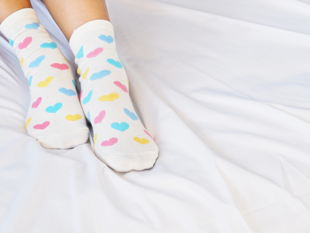 Close up woman feet wearing white sock with pastel heart shape pattern on bed in bedroom. Love...