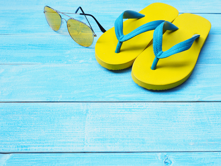 Top view of yellow rubber flip flop shoes and sunglasses on blue wooden background with copy space. Summer holiday vacation concept.の写真素材