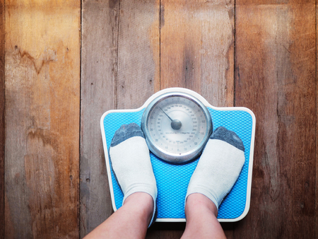 Girl feet standing on blue weight scale over wooden floor background.