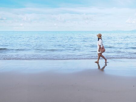 Asian woman walking relaxedly alone on sand along the beach in the morning. Happy summer holiday concept.の写真素材