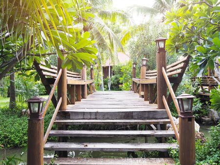 Wooden bridge crossing small canal at green garden decoration. Wood footpath at tropical resort.の写真素材