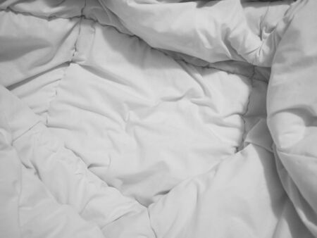 Close up crumpled white bedsheet and blanket surface in the morning at bedroom.の写真素材