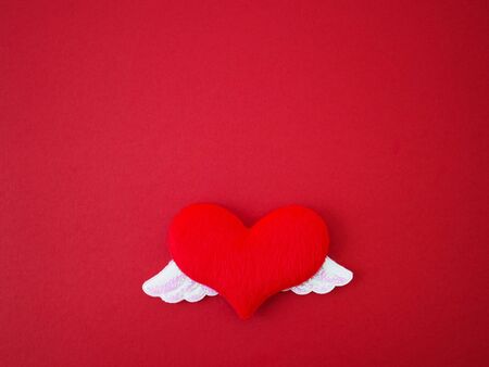 Close up soft red heart shape with two shiny white wings on red paper. Love concept for Valentine...