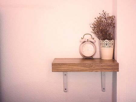 Retro pink alarm clock and dry flowers vase on wooden shelf in living room, vintage filter effect...
