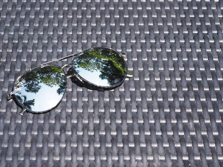 Close up sunglasses with reflection on lens over black weave chair next to swimming pool. Summer...