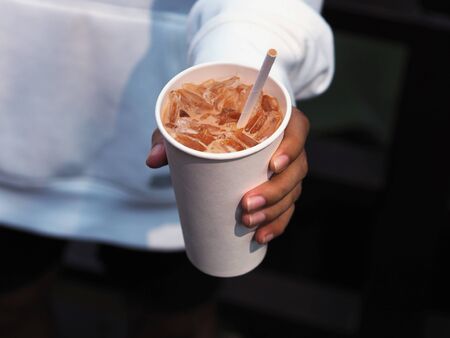 Top view disposable white recycling glass of cold cappuccino coffee with ice and paper straw in man...
