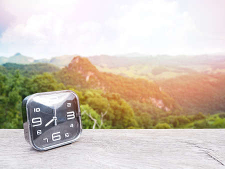 Close up clock on wooden table over green mountain and blue sky background.の写真素材