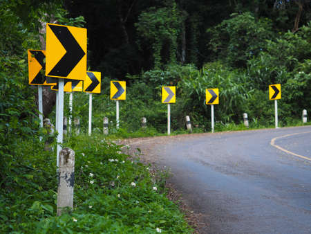 Curve warning sign on winding road in the forest for driving carefully.の写真素材