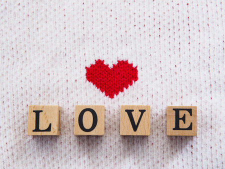 Love word text on wooden block over white fabric with red heart shape pattern for Valentine day or wedding background. Top view.の写真素材