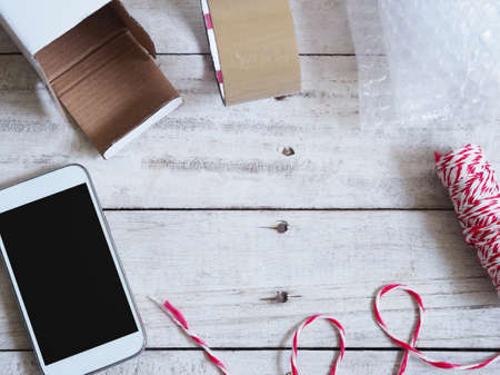 Mobile phone with box, tape, string and bubble on wooden table for entrepreneur preparing for...