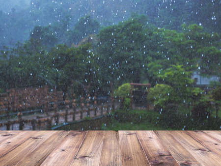 Wood table top over blurry heavy raining day in the park background. Montage style to display the...