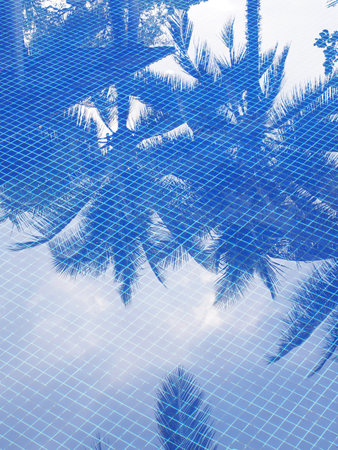 Reflection of coconut leaves trees in swimming pool with blue mosaic tiles.