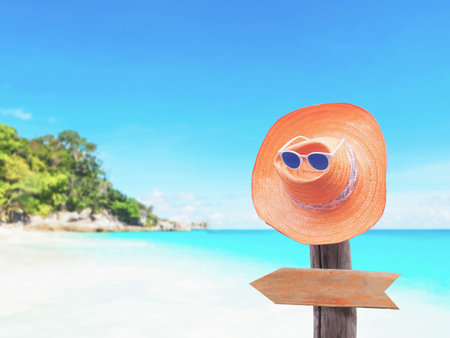 Vintage straw hat and blank brown wooden board arrow shape hanging on wood post over summer beach background. Happy holiday concept.の写真素材
